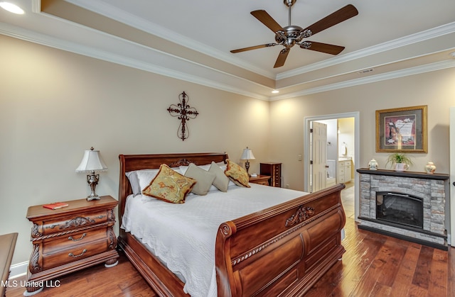 bedroom with a stone fireplace, ensuite bath, ceiling fan, ornamental molding, and a tray ceiling