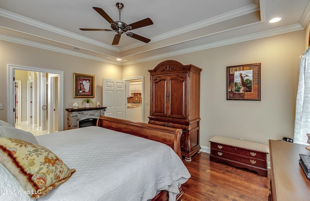 bedroom featuring dark wood-type flooring, ensuite bathroom, ceiling fan, ornamental molding, and a tray ceiling