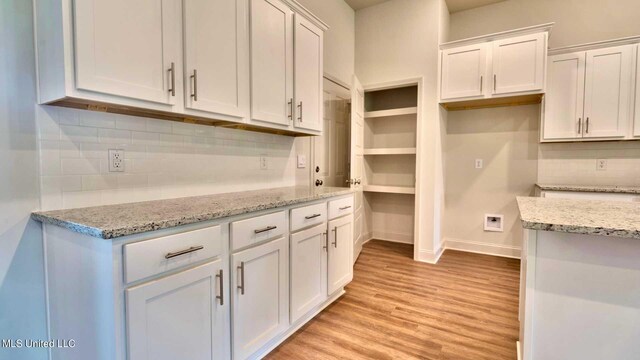 kitchen with light hardwood / wood-style flooring, white cabinetry, light stone countertops, and backsplash