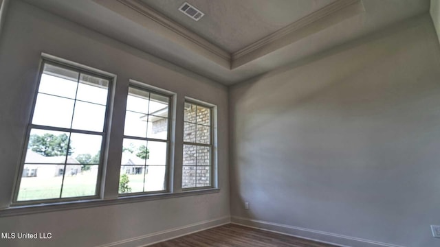 empty room with dark hardwood / wood-style flooring, crown molding, a tray ceiling, and plenty of natural light