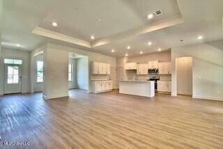 unfurnished living room with light hardwood / wood-style floors and a tray ceiling