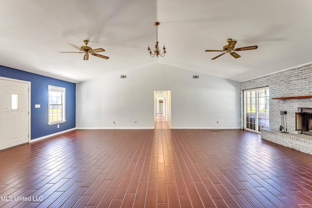 unfurnished living room with ceiling fan with notable chandelier, a wealth of natural light, and a brick fireplace