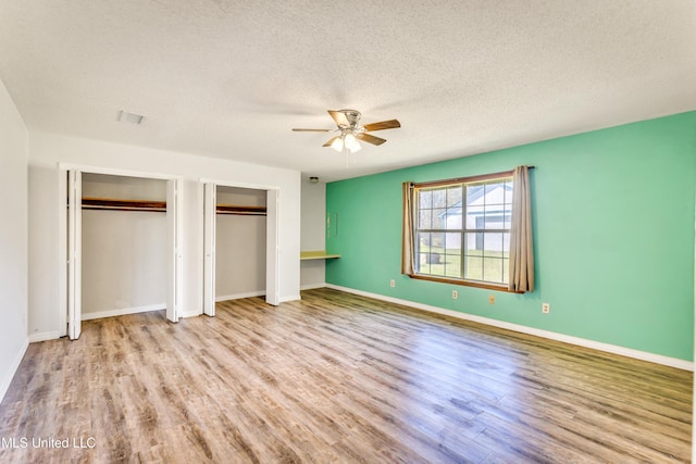 unfurnished bedroom featuring ceiling fan, light hardwood / wood-style floors, a textured ceiling, and two closets