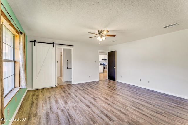 unfurnished bedroom with ceiling fan, a barn door, a textured ceiling, and light hardwood / wood-style flooring