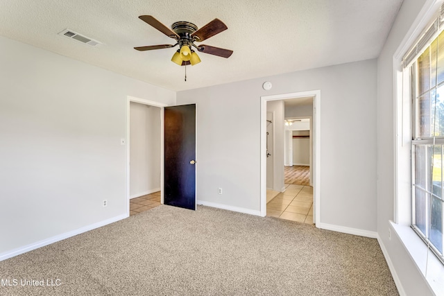 unfurnished bedroom with a textured ceiling, ceiling fan, light carpet, and multiple windows