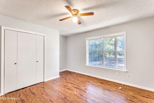 unfurnished bedroom with ceiling fan, wood-type flooring, a textured ceiling, and a closet