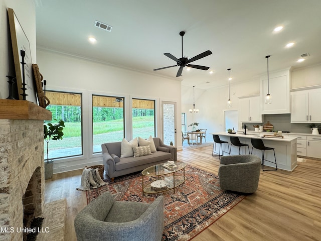 living room featuring ornamental molding, ceiling fan with notable chandelier, a fireplace, and light wood-type flooring