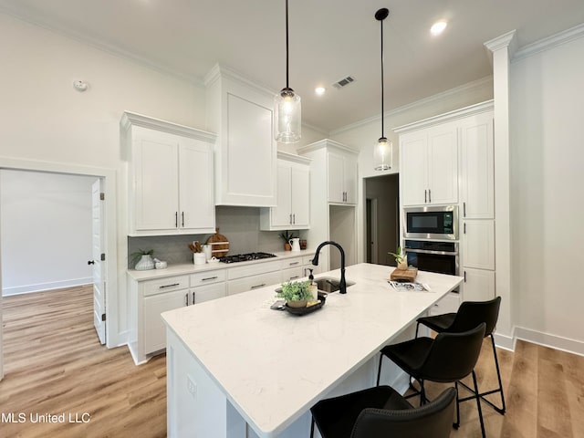 kitchen with sink, light wood-type flooring, stainless steel appliances, white cabinets, and a kitchen island with sink