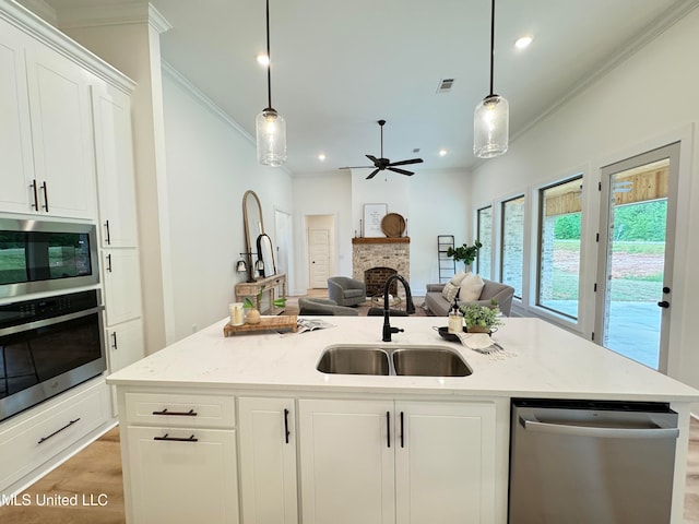 kitchen with a kitchen island with sink, a stone fireplace, sink, white cabinets, and appliances with stainless steel finishes