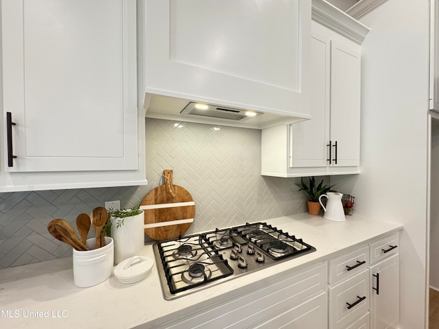 kitchen with custom exhaust hood, light stone countertops, stainless steel gas stovetop, white cabinetry, and tasteful backsplash