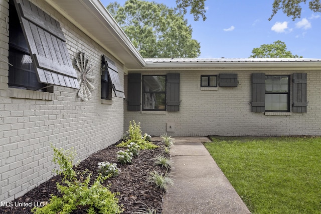 doorway to property with metal roof, brick siding, and a yard
