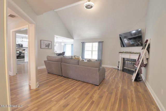 living room featuring an inviting chandelier, lofted ceiling, a tiled fireplace, and hardwood / wood-style floors