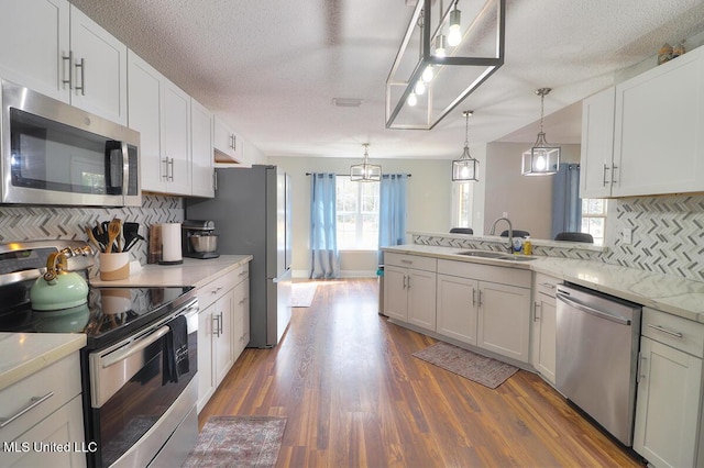 kitchen featuring sink, appliances with stainless steel finishes, dark hardwood / wood-style floors, pendant lighting, and white cabinets