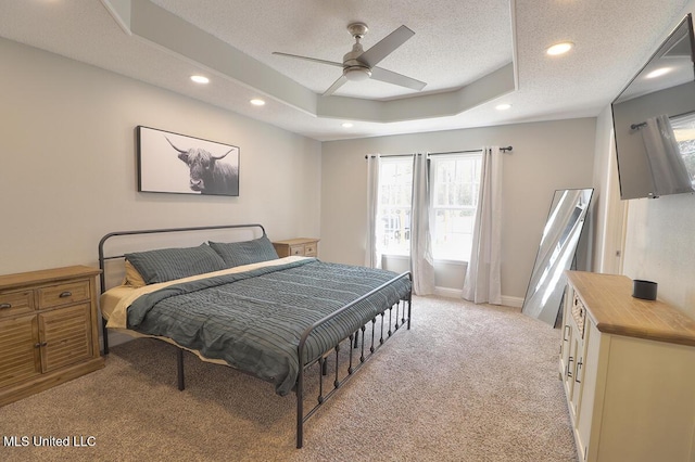 bedroom featuring ceiling fan, a tray ceiling, light colored carpet, and a textured ceiling