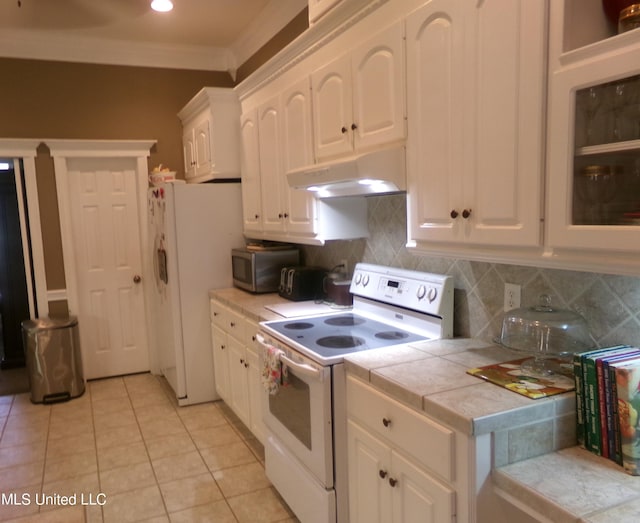 kitchen featuring white appliances, under cabinet range hood, tile countertops, white cabinets, and backsplash