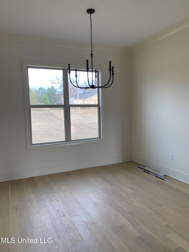 unfurnished dining area with a chandelier, light wood-type flooring, and crown molding