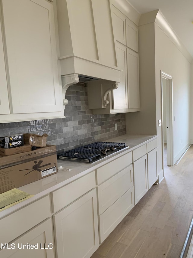 kitchen featuring decorative backsplash, premium range hood, stainless steel gas cooktop, light hardwood / wood-style flooring, and white cabinetry