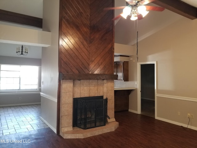 unfurnished living room featuring vaulted ceiling with beams, a tiled fireplace, dark hardwood / wood-style flooring, ceiling fan with notable chandelier, and wood walls