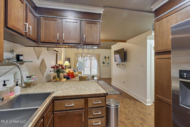 kitchen featuring stainless steel refrigerator with ice dispenser, a sink, light stone countertops, light wood-type flooring, and baseboards