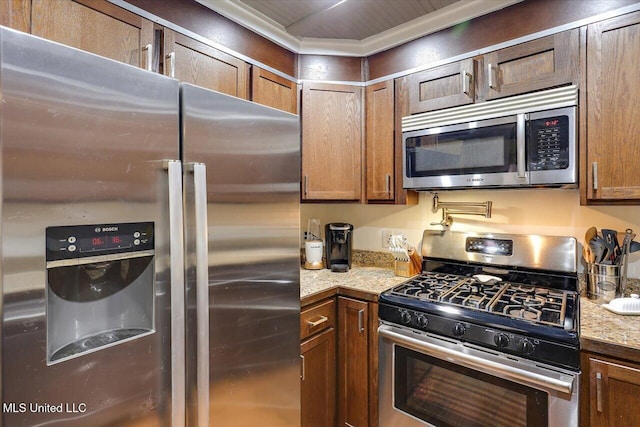 kitchen featuring stainless steel appliances, brown cabinets, and light stone countertops