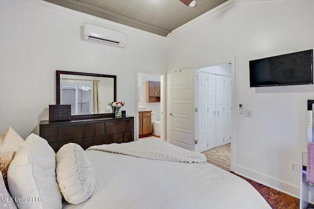 bedroom featuring baseboards, a wall unit AC, wood finished floors, ensuite bathroom, and a closet