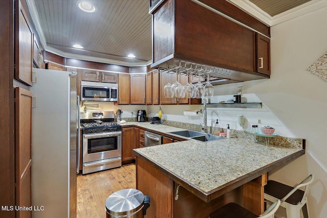 kitchen with light stone counters, a breakfast bar, a peninsula, stainless steel appliances, and a sink