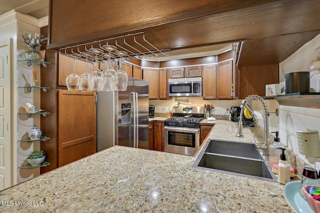 kitchen with appliances with stainless steel finishes, brown cabinets, a sink, and light stone counters