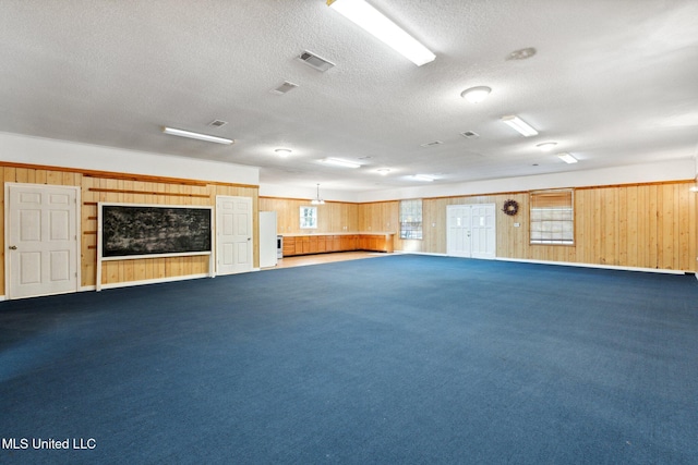 interior space with carpet, a textured ceiling, and wood walls