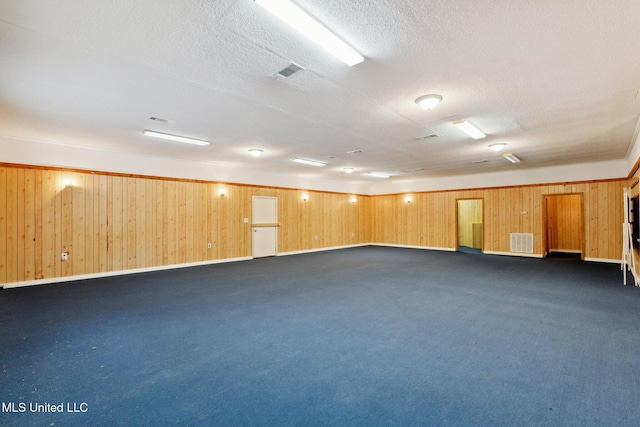 carpeted spare room with a textured ceiling and wood walls