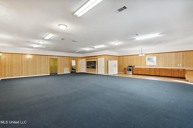 carpeted spare room featuring wood walls, a textured ceiling, and an inviting chandelier