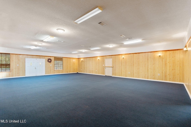 spare room with a textured ceiling, dark carpet, and wooden walls