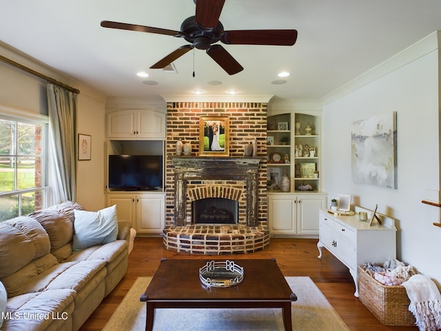 living room with ceiling fan, crown molding, wood-type flooring, built in features, and a fireplace