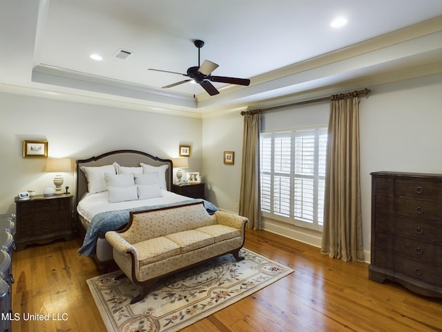 bedroom with hardwood / wood-style flooring, ceiling fan, and a raised ceiling