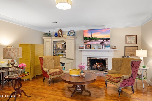 living area featuring crown molding, light hardwood / wood-style floors, and a brick fireplace