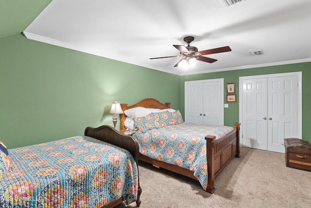 bedroom featuring ceiling fan, ornamental molding, light carpet, and two closets