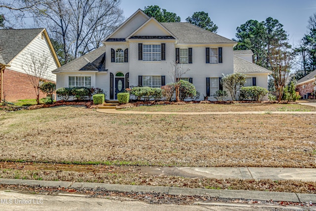 view of front facade featuring a shingled roof, a front yard, and brick siding