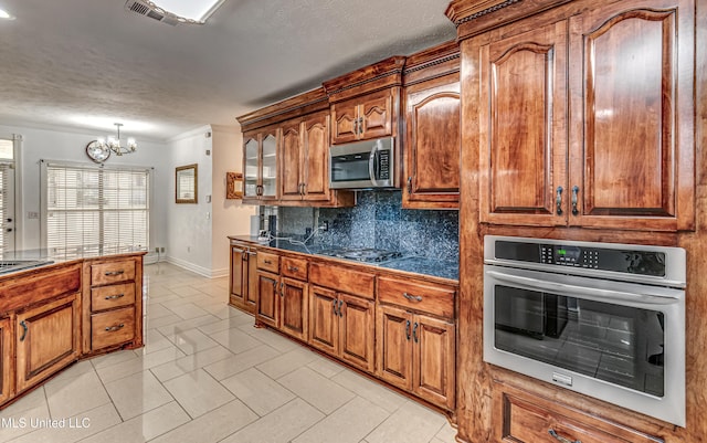 kitchen featuring visible vents, appliances with stainless steel finishes, backsplash, tile counters, and brown cabinets