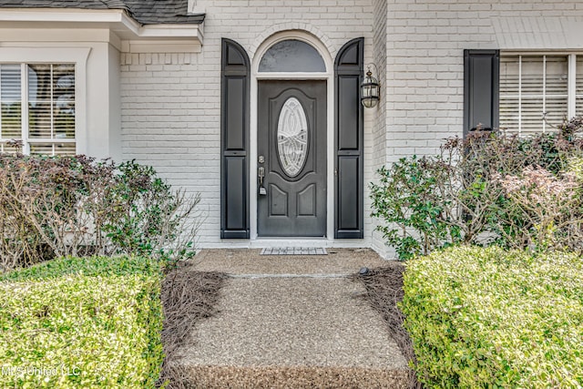 property entrance with a shingled roof and brick siding