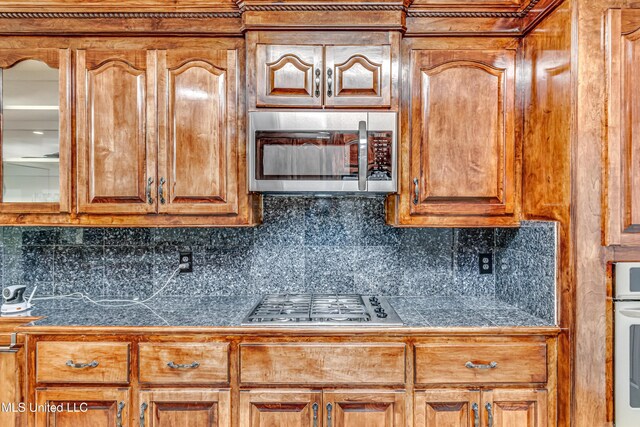 kitchen featuring brown cabinetry, tile countertops, glass insert cabinets, appliances with stainless steel finishes, and backsplash