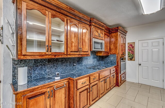 kitchen with tile countertops, stainless steel appliances, backsplash, brown cabinetry, and glass insert cabinets