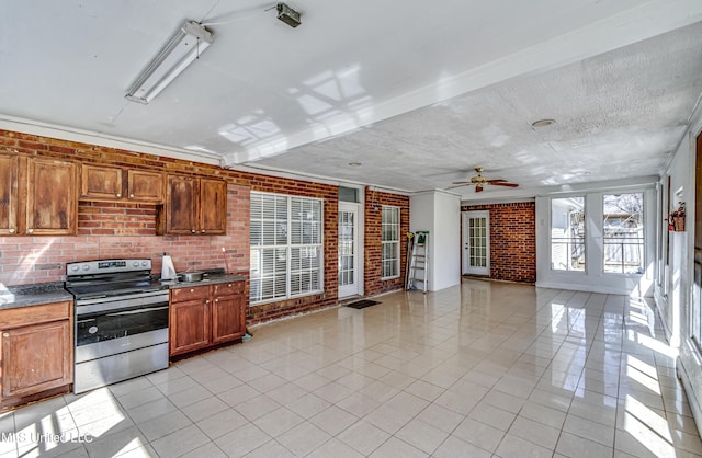 kitchen with light tile patterned floors, a textured ceiling, brick wall, stainless steel electric range oven, and dark countertops