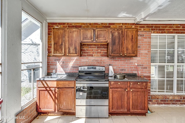 kitchen with light tile patterned floors, electric range, brown cabinetry, brick wall, and a sink