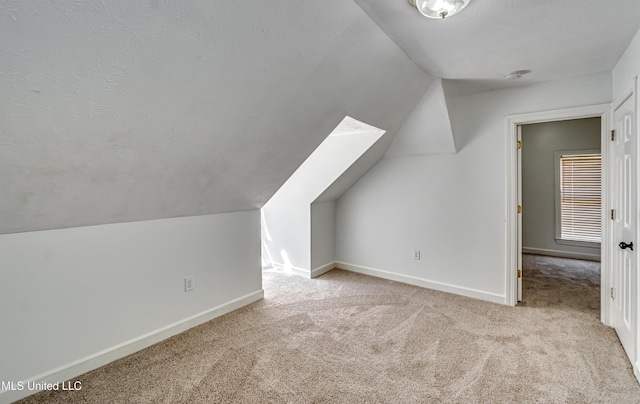 additional living space with lofted ceiling, carpet, a textured ceiling, and baseboards