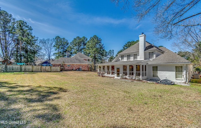 back of property with brick siding, a chimney, fence, and a yard