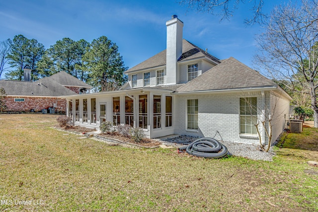 rear view of house with a lawn, a sunroom, a chimney, cooling unit, and brick siding