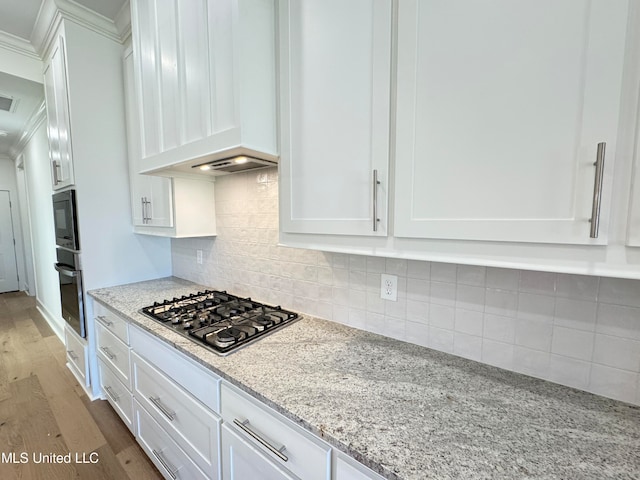 kitchen featuring stainless steel gas cooktop, light hardwood / wood-style flooring, backsplash, white cabinets, and light stone counters