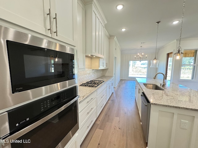 kitchen with sink, white cabinets, a healthy amount of sunlight, and an island with sink