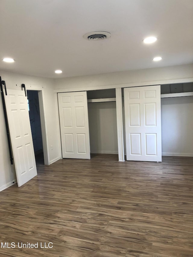 unfurnished bedroom featuring multiple closets, a barn door, and dark hardwood / wood-style flooring