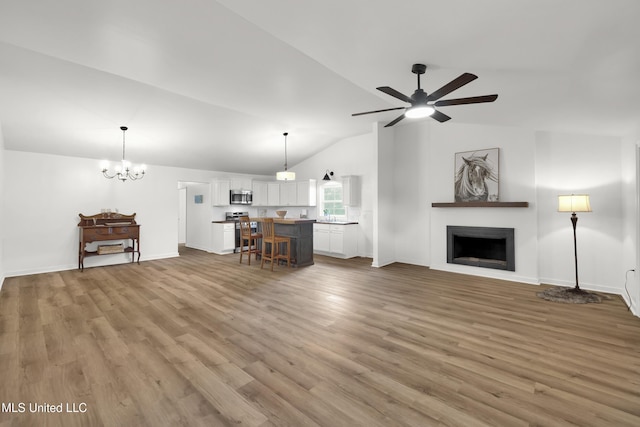 unfurnished living room featuring lofted ceiling, wood-type flooring, sink, and ceiling fan with notable chandelier