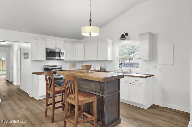 kitchen with sink, white cabinetry, wooden counters, vaulted ceiling, and hanging light fixtures